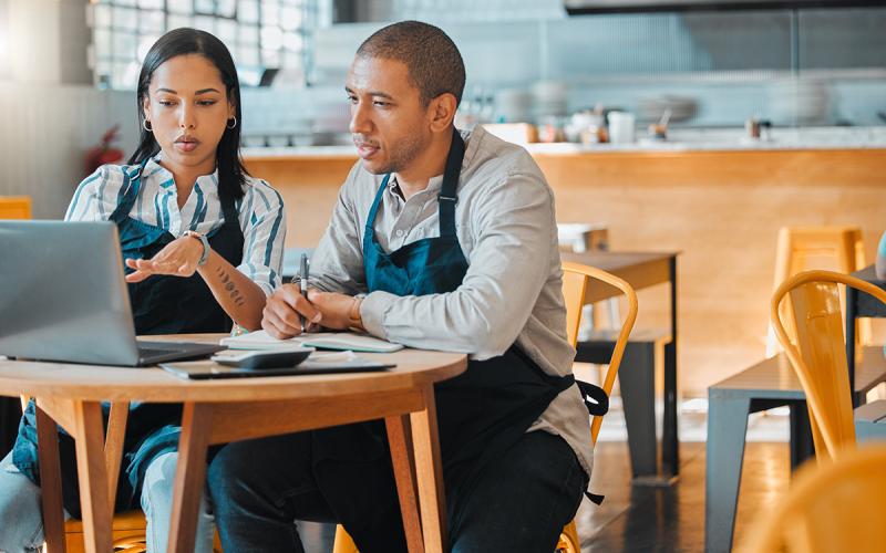 Small business cafe owners sitting at table with computer